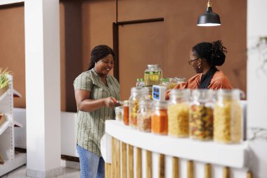 African american client at cashier desk purchasing homegrown organic produce at local food market. Cheerful black female customer assisted by friendly vendor at checkout counter in bio grocery shop. clipart