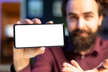 Çevrimiçi yayın kanalı logosunu göstermek için boş bir kopya alanı olarak kullanan insan eliyle izole edilmiş akıllı telefonu yakın çekim yap. Bulanık arkaplanda içerik oluşturucu tarafından tutulan model telefona odaklan
