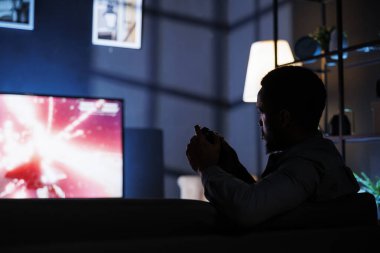 Afrikalı Amerikalı oyuncular internetten roket atarlı atış yarışması oynuyorlar, konsolu televizyonun içine takıyorlar ve arkadaşlarıyla geç saatlere kadar oyun oynuyorlar. Oyun oynayan genç adam.