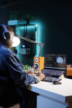 Mavi arayüzlü bir dizüstü bilgisayarda sinirsel bir ağ gösteren kulaklık kullanan bir kadın geliştirici. Siyahi kadın siber güvenliği yönetiyor ve gelecekteki veri merkezinde ağı izliyor..