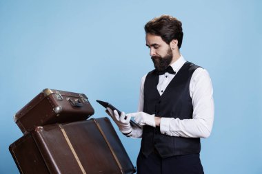 Doorman checks list on tablet, ensuring accommodation for all hotel guests. Young adult with suit and tie showcases hospitality industry concept, working as luxury bellhop with reservations. clipart