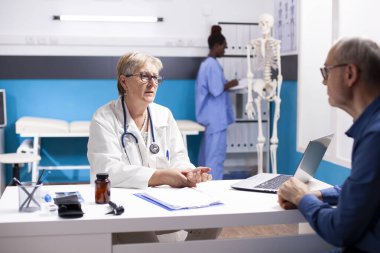 Klinik muayene sırasında emekli erkek hastalara tedavi seçenekleri sunan kıdemli bir doktor. Emekli kadın doktor hastane ofisindeki yaşlı adama tıbbi danışmanlık yapıyor..