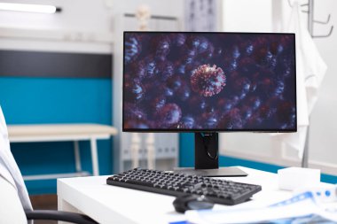 Devam eden tıbbi araştırmaları sembolize eden virüs hücrelerini gösteren masaüstü monitörünün seçici odağı. Modern bilgisayar, doktor randevusu için boş klinik masasına yerleştirildi..