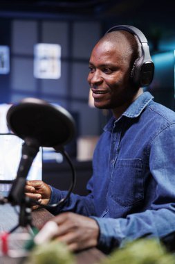 Evde online sohbet programı oluştururken mikrofona konuşan siyahi nüfuzlu kişi yakın planda gösteriliyor. Canlı yayın sırasında konuşan, kablosuz kulaklıklı bir blog yazarı podcast 'te tartışıyor.