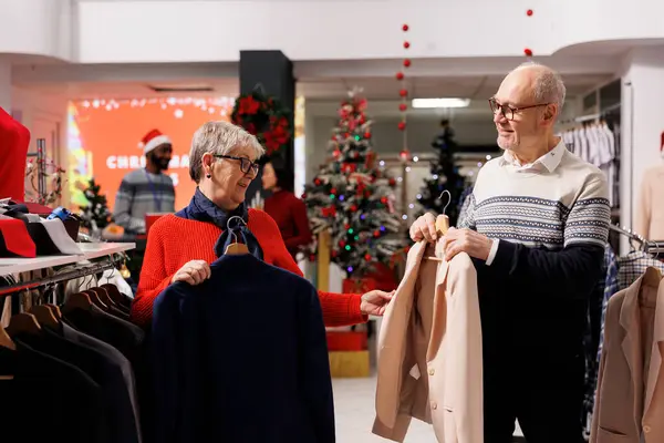 Yaşlı çift alışveriş merkezinde spor ceket arıyor, aile üyelerine Noel hediyesi almadan önce raflarda resmi kıyafet arıyorlar. İnsanlar tanıtım sezonunda alışveriş çılgınlığına devam ediyor..