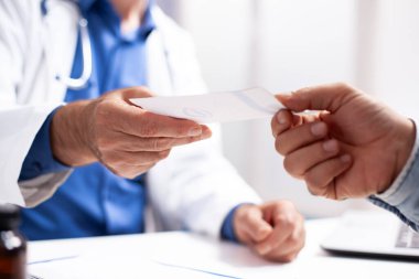 Yakın planda, hasta laboratuvar önlüklü doktordan yazılı iyileşme tavsiyesi alıyor, bakım ve tıbbi destek anı yakalıyor. Kafkasyalıların elinde reçete kağıtları var..