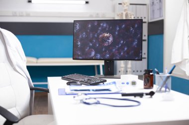 Araştırma amaçlı germ hücrelerini gösteren bilgisayar monitörlü boş bir tıbbi ofis, hastalığa karşı verilen mücadeleyi vurguluyor. Masaüstü bilgisayarı olan klinik odası grip virüsünün genişlemiş mikroskobik görüntüsünü gösteriyor.