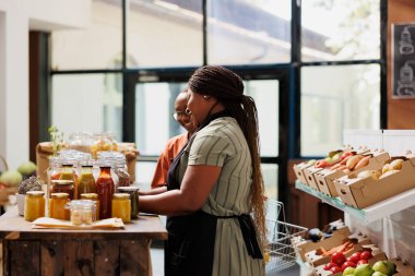 Afrikalı Amerikalı tüccar, onun çevre dostu dükkanında duruyor ve müşterilerine taze alınmış biyo-gıda ürünleri sunuyor. Kadın satıcı müşteriye hizmet ediyor, sürdürülebilir organik ürünlerini sergiliyor..