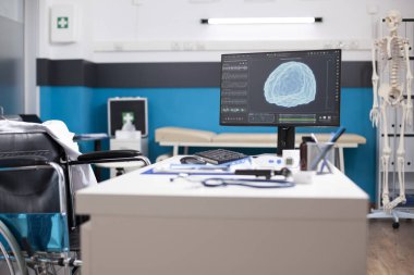 Masaüstü bilgisayarlı tekerlekli sandalye kullanıcı doktorları boş klinik odasında beyin görüntülerini gösteriyor. Sağlık değerlendirmeleri için ideal. Etkili hasta bakımı için araçlar, dosyalar ve teknoloji düzenlenmiştir.