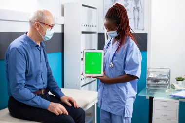 Siyah hemşire ve yaşlı beyaz adam yeşil ekran gösteren dijital cihaza bakıyor. Sağlık uzmanı emekli hastayla tıbbi sonuçları tartışıyor izole edilmiş telif alanı olan tablet kullanıyor..