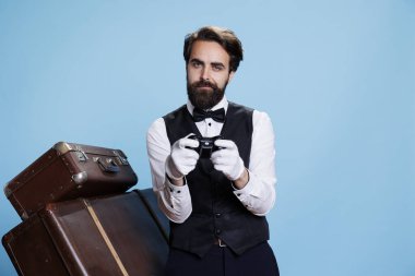 Doorkeeper posing with controller and playing videogames on the internet, feeling happy with gaming challenge in studio. Porter with suit and gloves has fun on camera, playing game. clipart