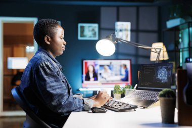 Masadaki Afrikalı Amerikalı kadın kişisel bilgisayarını programlama ve veri analizi için kullanıyor. Evde çalışan serbest çalışan kadın, laptopta bilgi teknolojisi ve veri merkezini etkin bir şekilde yönetiyor..