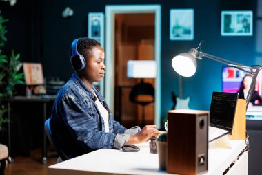 Laptopta çalışan Afro-Amerikalı kadın, radyo kulaklıkla müzik dinlerken programlama kodu. Sistem yazılımını izlemek için kişisel bilgisayar kullanan kulaklıklı kadın bir serbest yazar.