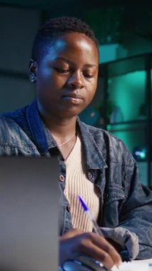 Ev ofisinin bilgisayarında çalışan dikey video girişimcisi internete göz atıyor ve not defterine yazıyor. Telgraf çekilirken kalem, not defteri ve dijital aygıt kullanan kadın, kamera B