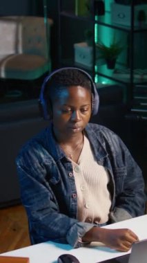 Dikey video Freelancer, kişisel ev ofisinde müzik dinlerken takım projesi için bilgisayar görevleri yapıyor. Uzaktan çalışan, gece geç saatlere kadar çalışan, dizüstü bilgisayarda yazan, kulaklık takan biri.