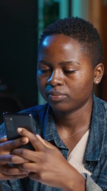 Dikey videolu neşeli kadın ofis masasında oturmuş bilgisayarın önünde arkadaşlarına akıllı telefondan mesaj atıyor. Neşeli serbest çalışan arkadaşlarıyla sohbet etmek için internetten telefon kullanıyor.