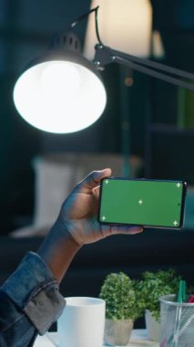 Dikey video işi yapan kadın krom tuşlu akıllı telefon kullanırken dizüstü bilgisayardaki istatistikleri kontrol ediyor. İzole edilmiş ekranlı telefonu peyzaj modunda tutan uzaktan çalışan, iş grafiklerini analiz ediyor