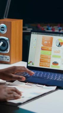 Evden çalışan dikey video girişimcisi, dizüstü bilgisayar kullanıyor, kağıda notlar yazıyor. Kişisel apartman ofisindeki uzaktan çalışan önemli bilgileri not defterine yazıp istatistiklere bakıyor.