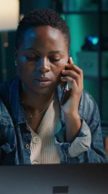 Ev bilgisayarında kişisel ofiste çalışırken, arkadaşından telefon alan dikey videolu kadın. Freelancer görev çözerken cep telefonu kullanarak arkadaşla konuşuyor, kamera A