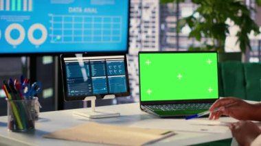 Genç genel müdür laptopta yeşil ekran kullanıyor ve personeli için performans ölçümlerini değerlendiriyor, bir planlama oturumu düzenliyor. Afrikalı Amerikalı CEO liderlik becerileri gösteriyor. Kamera A.