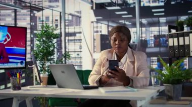 Afrika kökenli Amerikalı genel müdür performans ölçümlerini tartışmak ve iş geliştirme projesine odaklanmak için akıllı telefon çağrılarına cevap veriyor. Direktör, günlük işlemleri ve analizleri yapıyor. Kamera B.