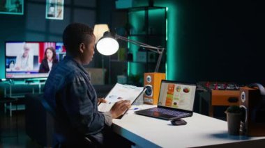 Kişisel ofiste çalışan serbest çalışan bir kadın dizüstü bilgisayardaki istatistiksel veri finans grafiklerini kontrol ediyor. Uzaktan kumandalı çalışan oturma odasında iş dünyasının grafiksel rakamlarını karşılaştırıyor, kamera B