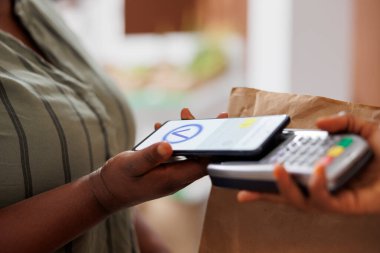 Afro-Amerikan bir müşterinin kasada banka kartıyla ödeme yaparken çekilmiş ayrıntılı bir resmi. Müşterinin ödemesini yapması için kadın satıcının elinde makineyle yakın plan fotoğrafı..