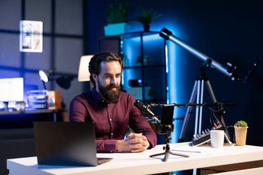 İnternetteki yıldız tripoda bağlı akıllı telefondan konuşuyor ve stüdyoda yüksek kalitede mikrofon izleyicilerle tartışıyor. Sosyal medya videosu kaydetmek için cep telefonu ve profesyonel ekipman kullanan bir adam