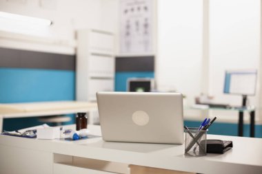 Dijital dizüstü bilgisayar doktor ofisinde masanın üzerinde. Tıbbi ekipman ve modern cihazların bulunduğu boş bir hastane odası..