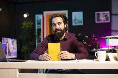 Stüdyodaki adam sesli kayıt üzerinde çalışıyor, kitaptan okuyor, profesyonel mikrofonla ses kaydediyor. Özel donanımlı internet yayıncıları için ses aktörü kitabı hazırlıyor
