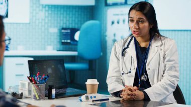 Uzman ve hasta modern bir muayenehanede teşhis sonuçlarını tartışıyor, röntgen görüntüleme sonuçları ve MRI taramaları sunmak için gelişmiş sağlık teknolojisi kuruluyor. Bakım yönetimi. Kamera A.