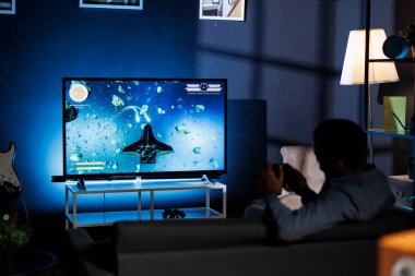 Geceleri video oyunu oynayan odaklanmış kişi, uzun menzilli silahlarla online çok oyunculu rekabete giriyor. Afrika kökenli Amerikalı inek roket oyunlarıyla eğleniyor..