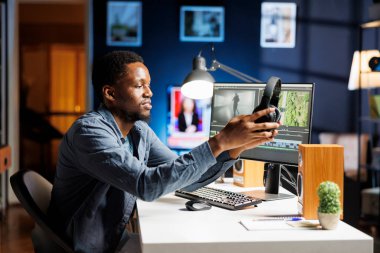 Film yapımcısı, çalışma masasında post prodüksiyon arayüzü kullanarak video görüntülerini düzenliyor. Renklendirme ve beyaz denge ayarları ile çalışan serbest kameraman.