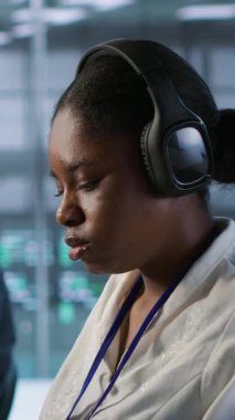 Bilgi işleme gereksinimlerini optimize etmek için sunucu çiftliğinde çalışırken zamanın daha hızlı geçmesi için gülümseyen mühendis işitme podcast 'lerinin dikey video portresi. Mutlu kadın verilerle şarkıları dinliyor.