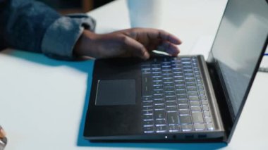 Evden çalışan bir tele-işçi, dizüstü bilgisayarda klavye kullanıyor, belge yazıyor. Uzaktan çalışan klavyedeki tuşlara basıyor, iş ortaklarına e-posta gönderiyor, kamera A yakın plan