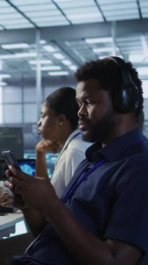 Sunucu odasında cep telefonu kullanan dikey video yöneticisi. en az arayı sağladıktan sonra rahatlıyor. Veri merkezi bilişim uzmanı akıllı telefondan mesaj atıyor, izleme performansına ara veriyor, kamera A