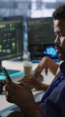 Sunucu odasında cep telefonu kullanan dikey video yöneticisi. en az arayı sağladıktan sonra rahatlıyor. Veri merkezi bilişim uzmanı akıllı telefondan mesaj atıyor, izleme performansına ara veriyor, kamera A