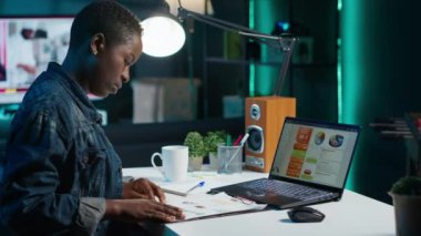 Kişisel ofiste çalışan serbest çalışan bir kadın dizüstü bilgisayardaki istatistiksel veri finans grafiklerini kontrol ediyor. Uzaktan kumandalı çalışan oturma odasında iş dünyasının grafiksel figürlerini karşılaştırıyor.