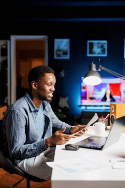 Arşivlenmiş belgelerin istatistiklerini inceleyen işletme öğrencisi, yürütme sorumluluklarını çözmeyi ya da mali konular üzerinde çalışmayı öğreniyor. Afrikalı Amerikalı müteahhit evde rapor ve terimler okuyor..