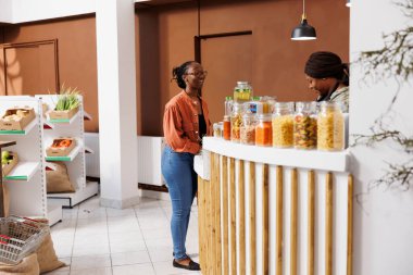 An African American woman and vendor talking about locally grown, organic fruit at grocery store checkout counter. Conscious consumer supporting sustainability and zero waste. clipart