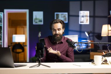 Teknoloji uzmanı cep telefonu performansını değerlendiriyor, içeride kullanılan parçalardan bahsediyor. Teknoloji internet kanalında incelemek için cep telefonu paketlerini açan eğlence aracı, profesyonel mikrofonla kayıt yapıyor