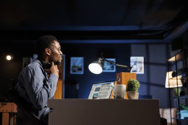 Afrikalı Amerikalı analist maliyet ve gelir unsurlarını online istatistik raporunda inceliyor, yeni sermaye fonları elde etmek için evden çalışıyor. Bilgisayarda mali kayıtları inceleyen genç bir yetişkin..