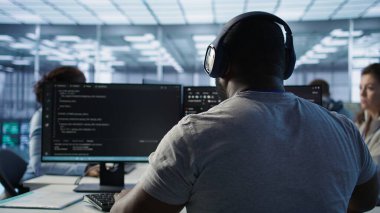 Bilgisayar ağı güvenlik veri merkezinde çalışan bir sistem yöneticisi müzik dinliyor. Kulaklık takan Afrikalı Amerikalı işçiler sunucuları izliyorlar enerji tüketimini rafa kaldırıyorlar, kamera B