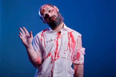 Cadılar bayramı için kana bulanmış uğursuz zombi kılığındaki bir adamın resmi. Kameraya el sallıyor. Korkunç makyaj yapan, vahşi hortlak gibi davranan, stüdyo geçmişi olan biri.