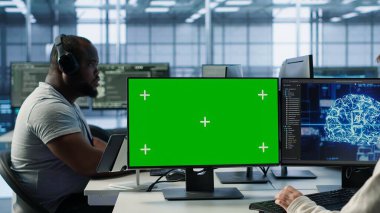 Yapay zeka veri merkezindeki IT çalışanları yeşil ekran bilgisayarlarda kodlama, güncelleme ekipmanları. Bilgisayar masasındaki mühendislerden oluşan çok ırklı bir ekip sunucu kümelerini görüntüleme monitörleri ve kamera A kullanarak denetliyor.