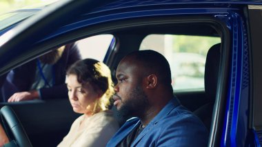 Müşteriler araba almadan önce test sürüşü yapıyorlar, pedal ve koltuk ayarlarının uygun ve rahat olup olmadığını kontrol ediyorlar. Karı koca yeni bir araç satın alıyor. Nasıl hissettirdiğini değerlendiriyorlar. Kamera A: