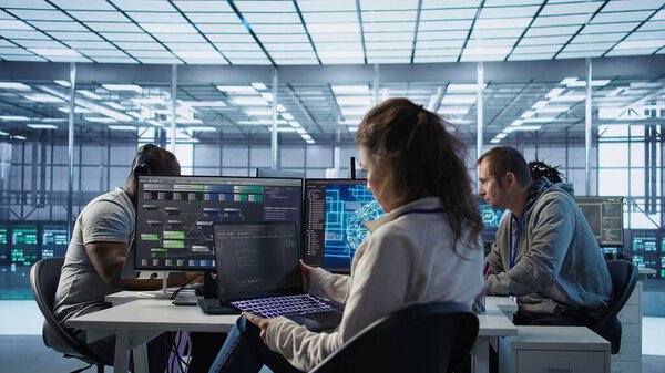 IT employee programming in AI server farm housing advanced equipment used for machine learning training. Admin running code on laptop to upgrade artificial intelligence rigs, camera B