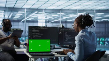 Sunucu merkezindeki çeşitli geliştiriciler yeşil ekran laptopunu kullanarak yanlış yapılandırmaları arıyorlar. Afrika kökenli Amerikalı bilişim uzmanları veri merkezi hatalarını kroma anahtar not defteri, kamera B ile onarıyor.