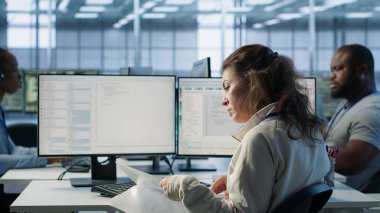 Çalışanların sunucu odasını denetlemesi, evrak okuması, sorun çıkaran donanım. Denetmen sunucu merkezinde inceleme yapıyor, bilgisayar masasında teknik dosyaları okuyor, kamera A