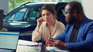 Galerideki müşteriler araba satışıyla ilgili gerekli ödeme belgelerini tamamlıyorlar, düzgün işlemler için finans ve sigorta departmanlarıyla işbirliği yapıyorlar, kamera A